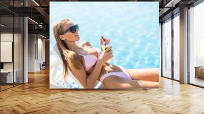 Young sexy woman relaxing at the poolside with pina colada cocktail Wall mural